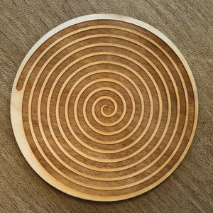 Könnte beinhalten: Ein Untersetzer aus Holz mit einem Spiraldesign. Der Untersetzer ist aus hellbraunem Holz gefertigt und hat eine natürliche Oberfläche.