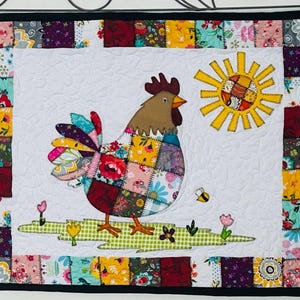 May include: A quilted wall hanging featuring a colorful rooster with a patchwork body, a yellow sun, and a bee. The rooster stands on a green and white stitched ground with flowers. The border is made of floral patchwork.