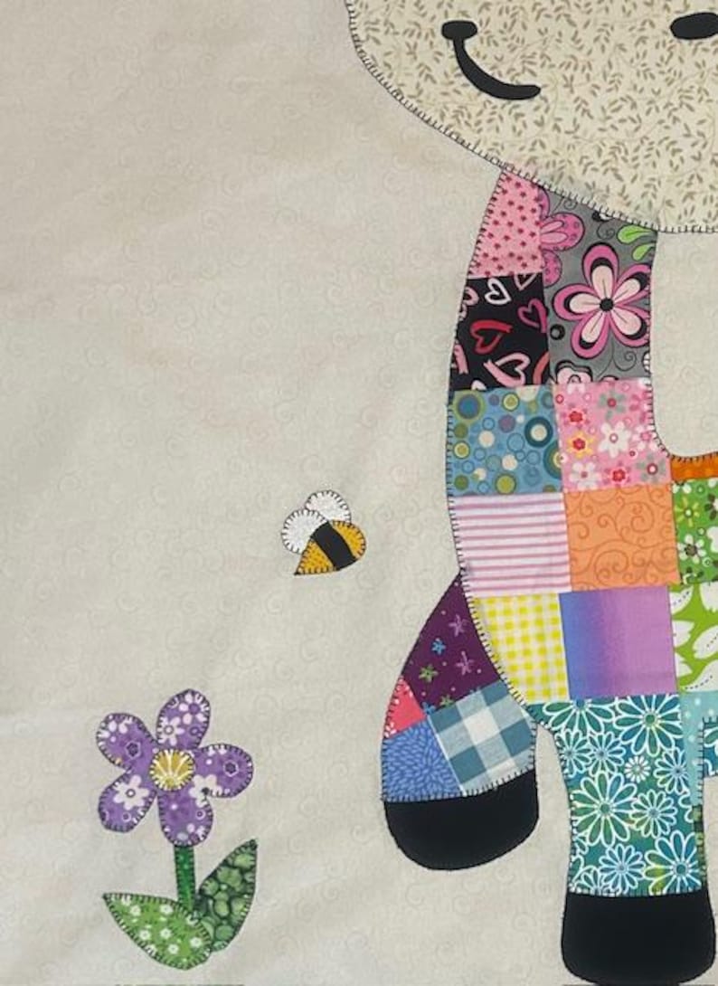 May include: A colorful patchwork giraffe with a smiling face, a bee, and a flower. The giraffe's body is made of various patterned fabrics, including floral, hearts, and stripes. The background is a light cream color.