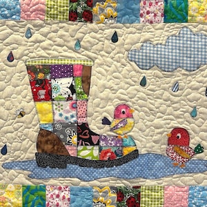 May include: A patchwork fabric rain boot with a blue puddle underneath. Two colorful birds are perched on the edge of the puddle. A blue and white gingham cloud is in the upper right corner of the image. The background is a cream colored fabric with a quilted texture.