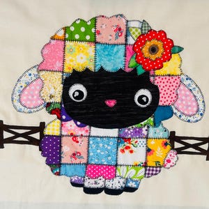 May include: A whimsical patchwork sheep design with a black face, large eyes, and a pink heart-shaped nose. The sheep's wool is made of colorful squares, and it wears a red flower. A small bee and a brown fence are also present.