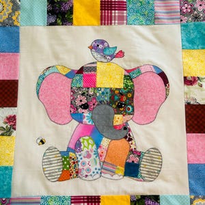 May include: A colorful patchwork quilt featuring a whimsical elephant design. The elephant is made of various patterned fabrics, with pink ears and a gray trunk. A small bird sits atop the elephant's head, and a bee is nearby. The quilt is bordered with assorted fabric squares.