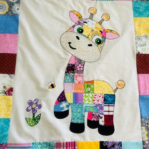 以下が含まれることがあります： 手作りのパッチワークキルト。気まぐれなキリンのアップリケが特徴です。キリンはカラフルな布の正方形で構成され、笑顔の顔、蜂、花がアクセントになっています。キルトの縁は、さまざまな模様の生地のストリップで作られています。