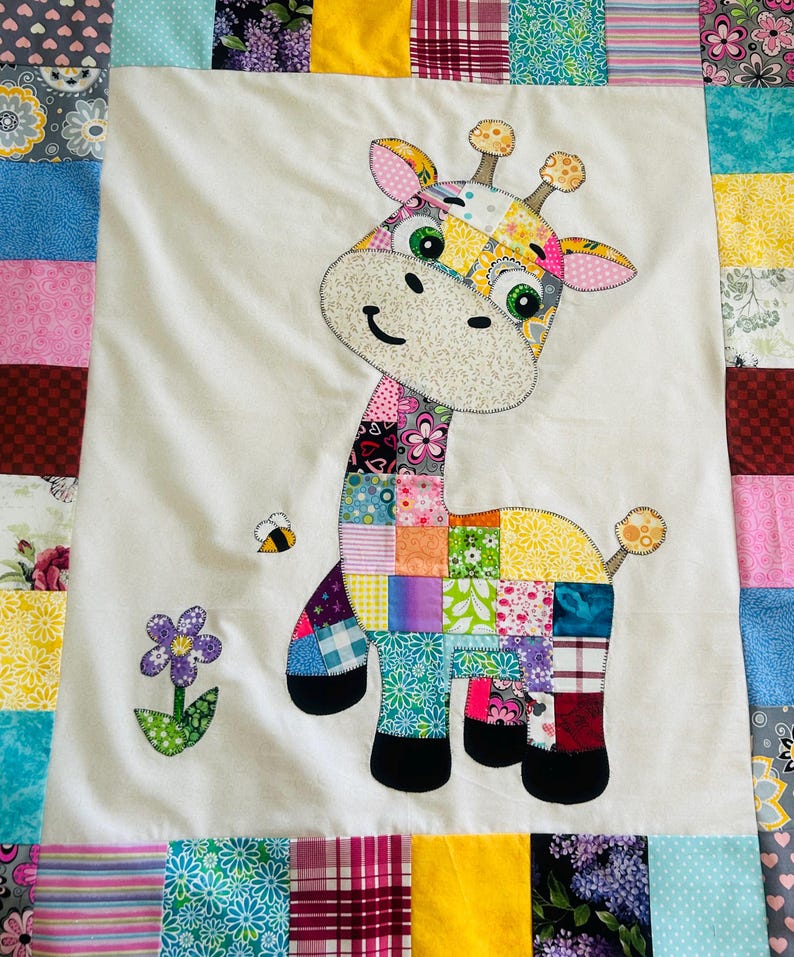 May include: A handmade patchwork quilt featuring a whimsical giraffe applique. The giraffe is composed of colorful fabric squares, with a smiling face, and a bee and flower accent. The quilt's border is made of various patterned fabric strips.