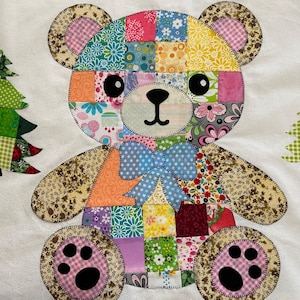 May include: A patchwork teddy bear with a blue bow tie, black eyes, and pink paw prints. Two patchwork Christmas trees flank the bear. The bear is made from various patterned fabrics, creating a vibrant design.