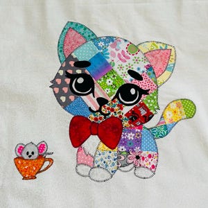 May include: A colorful patchwork cat with a red bow tie and large, expressive eyes. A small mouse in an orange teacup is to the left of the cat. The cat and mouse are made of various patterned fabrics.