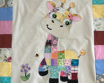 May include: A colorful patchwork giraffe applique on a white background, surrounded by a patchwork border. The giraffe has a smiling face, green eyes, and is accompanied by a bee and a flower. The quilt is a charming handmade item.