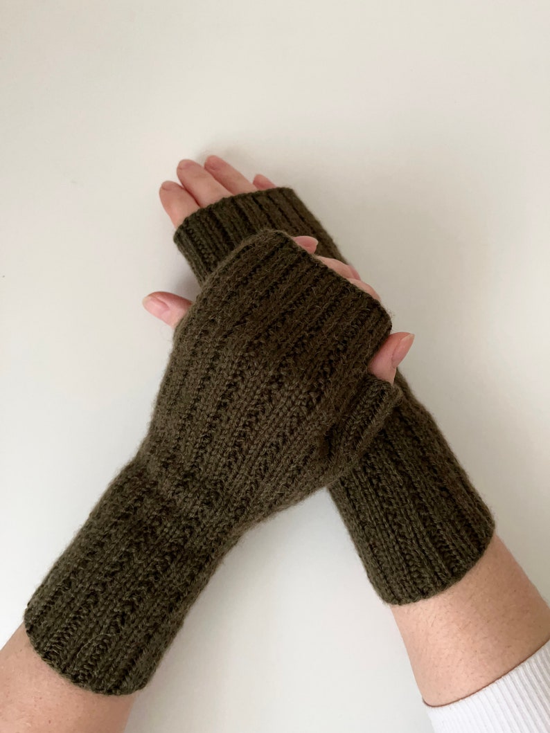 May include: A pair of olive green fingerless gloves made of knitted wool. The gloves are folded over and the cuffs are visible.