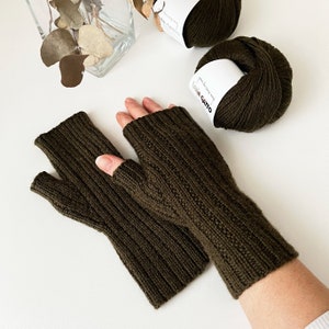 May include: A pair of olive green fingerless gloves with a cable knit pattern. The gloves are made with Lana Gatto yarn.