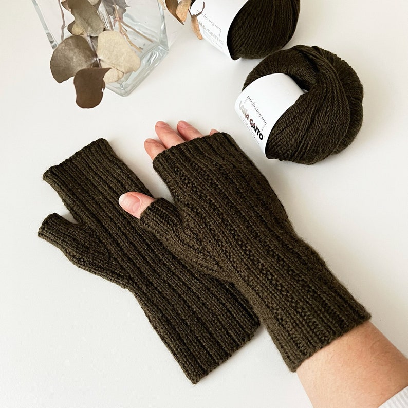 May include: A pair of olive green fingerless gloves with a cable knit pattern. The gloves are made with Lana Gatto yarn.