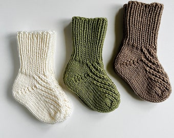 May include: Three pairs of knitted baby socks in white, green and brown.