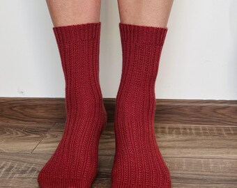 May include: A pair of ribbed knit socks in a deep red hue. The socks are mid-calf length and have a textured pattern. The socks are displayed on a wooden floor.