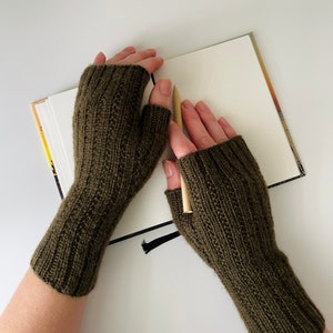 May include: A pair of olive green fingerless knitted gloves. The gloves are made of a soft, warm material and are perfect for keeping your hands warm in the winter.
