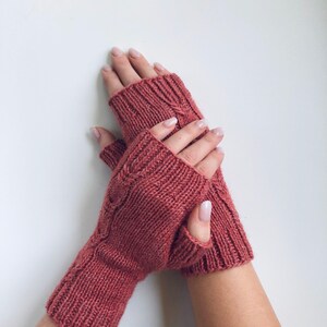 May include: A pair of pink knitted fingerless gloves with a cable knit pattern.