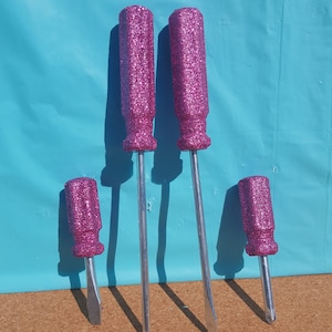 May include: Four pink glitter screwdrivers with silver metal shafts. The screwdrivers are different sizes.