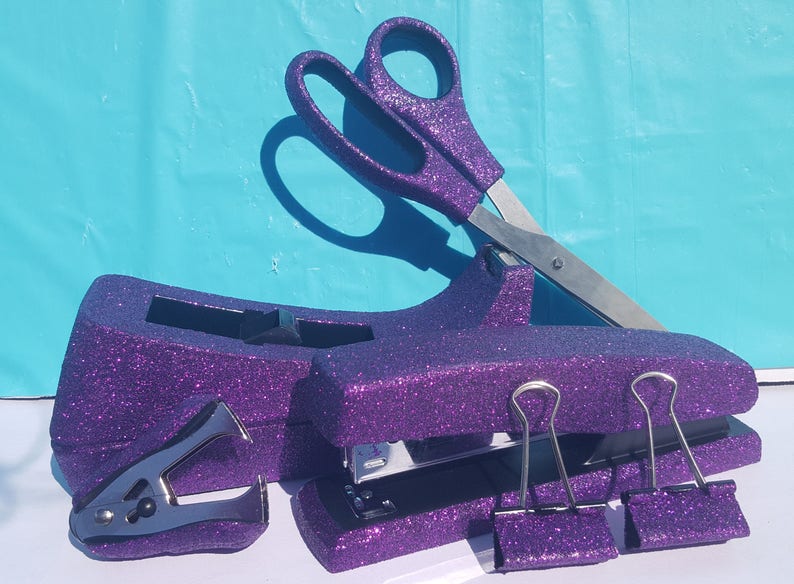May include: Purple glitter desk organizer set with a stapler, staple remover, scissors, and two binder clips.