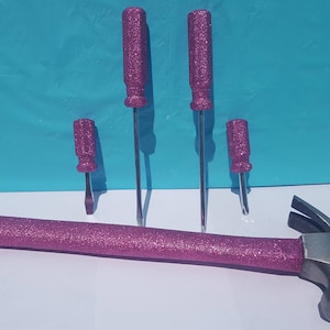 May include: A set of four pink glitter screwdrivers and a pink glitter hammer. The screwdrivers have different sizes and the hammer has a silver head.