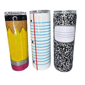 May include: Three stainless steel tumblers with glitter finishes. The tumblers are decorated with a pencil, notebook paper, and a notebook cover design.
