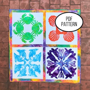 Może przedstawiać: Wzór PDF do kołdry z czterema różnymi motywami morskimi: zielonym krabem, pomarańczową muszlą, niebieskim delfinem i fioletowym koralem. Bloki kołdry są umieszczone na białym tle z kolorową ramką.