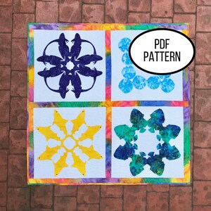Könnte beinhalten: Ein Quiltblockmuster mit vier verschiedenen Designs. Die Designs bestehen aus Fischen, Fröschen und geometrischen Formen. Der Quiltblock ist aus buntem Stoff mit einem Batik-Effekt gefertigt. Der Text "PDF PATTERN" ist im Bild sichtbar.