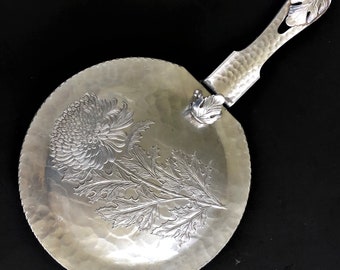 May include: A silver serving tray with a hammered finish and a floral design. The tray has a removable handle with a leaf design.