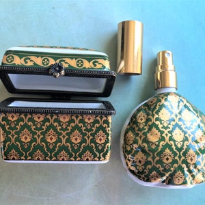 May include: An open, rectangular trinket box and a perfume bottle with a gold and green damask pattern. The box has a hinged lid and a dark metal frame. The perfume bottle has a gold cap and sprayer.