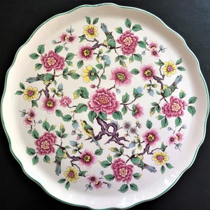 May include: A white ceramic serving platter with a scalloped edge and a green trim. The platter features a floral design with pink and yellow flowers, green leaves, and small yellow birds.