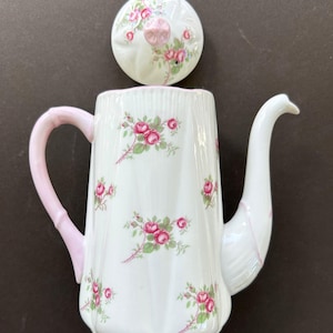 May include: White porcelain teapot with a pink handle and spout, decorated with pink roses and green leaves. The lid is also white with a pink rose design. The teapot has a fluted design.