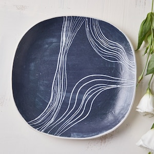 May include: A blue ceramic plate with white abstract lines. The plate is oval shaped and has a glossy finish.