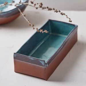 Könnte beinhalten: Eine rechteckige Keramikschale mit einer türkisfarbenen Glasur und einem braunen Rand. Die Schale steht auf einer weißen Oberfläche.