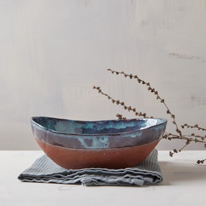 May include: A handmade ceramic bowl with a blue and brown glaze. The bowl is sitting on a gray linen napkin.