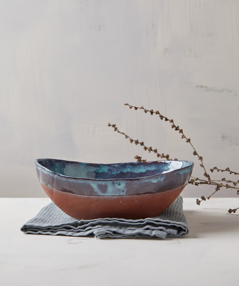 May include: A handmade ceramic bowl with a blue and brown glaze. The bowl is sitting on a gray linen napkin.