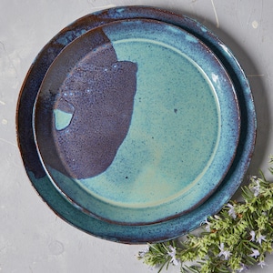 Op de afbeelding: Een set van twee keramische borden met een blauwe en bruine glazuur. De borden zijn op elkaar gestapeld.