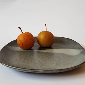 Puede incluir: Dos pequeñas peras redondas de color amarillo con tallos marrones sobre un plato de cerámica gris con una franja blanca.