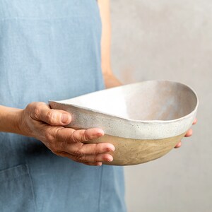 May include: A person holding a large, oval-shaped ceramic bowl with a white glaze and a brown base.