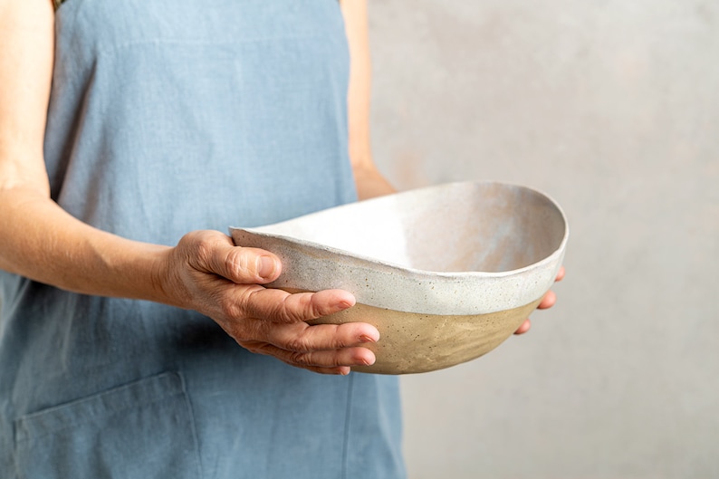 May include: A person holding a large, oval-shaped ceramic bowl with a white glaze and a brown base.