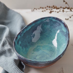 May include: A teal blue ceramic bowl with a dark brown rim. The bowl is sitting on a white surface.