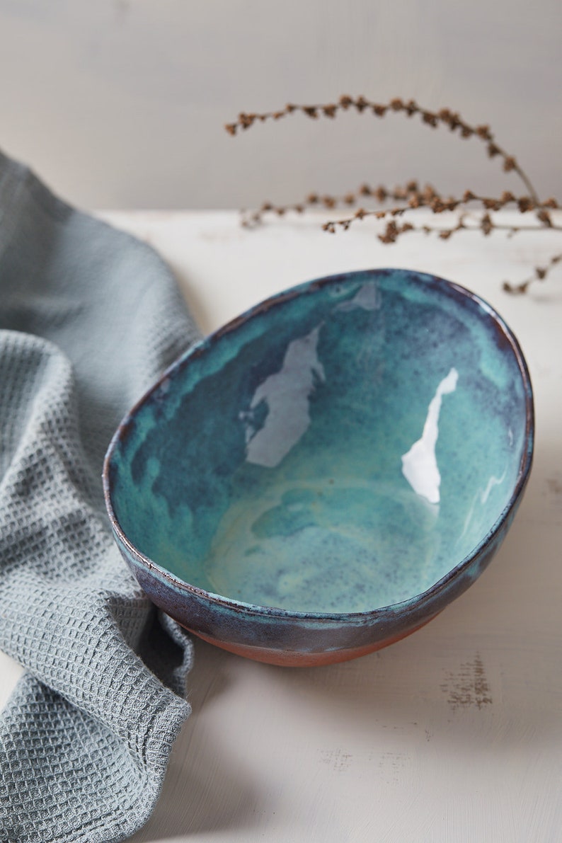 May include: A teal blue ceramic bowl with a dark brown rim. The bowl is sitting on a white surface.