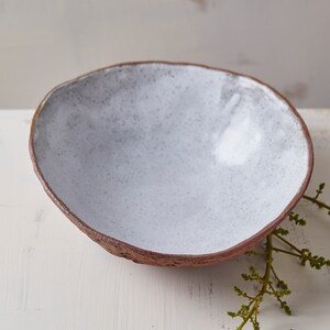 May include: A white ceramic bowl with a rough, textured exterior. The bowl is empty and sits on a white surface.