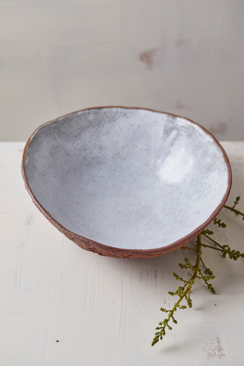 Op de afbeelding: Een witte keramische kom met een ruw, getextureerd exterieur. De kom is leeg en staat op een wit oppervlak.