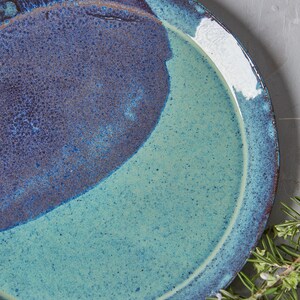 May include: A ceramic plate with a blue and green glaze. The plate has a speckled finish and a rounded rim.