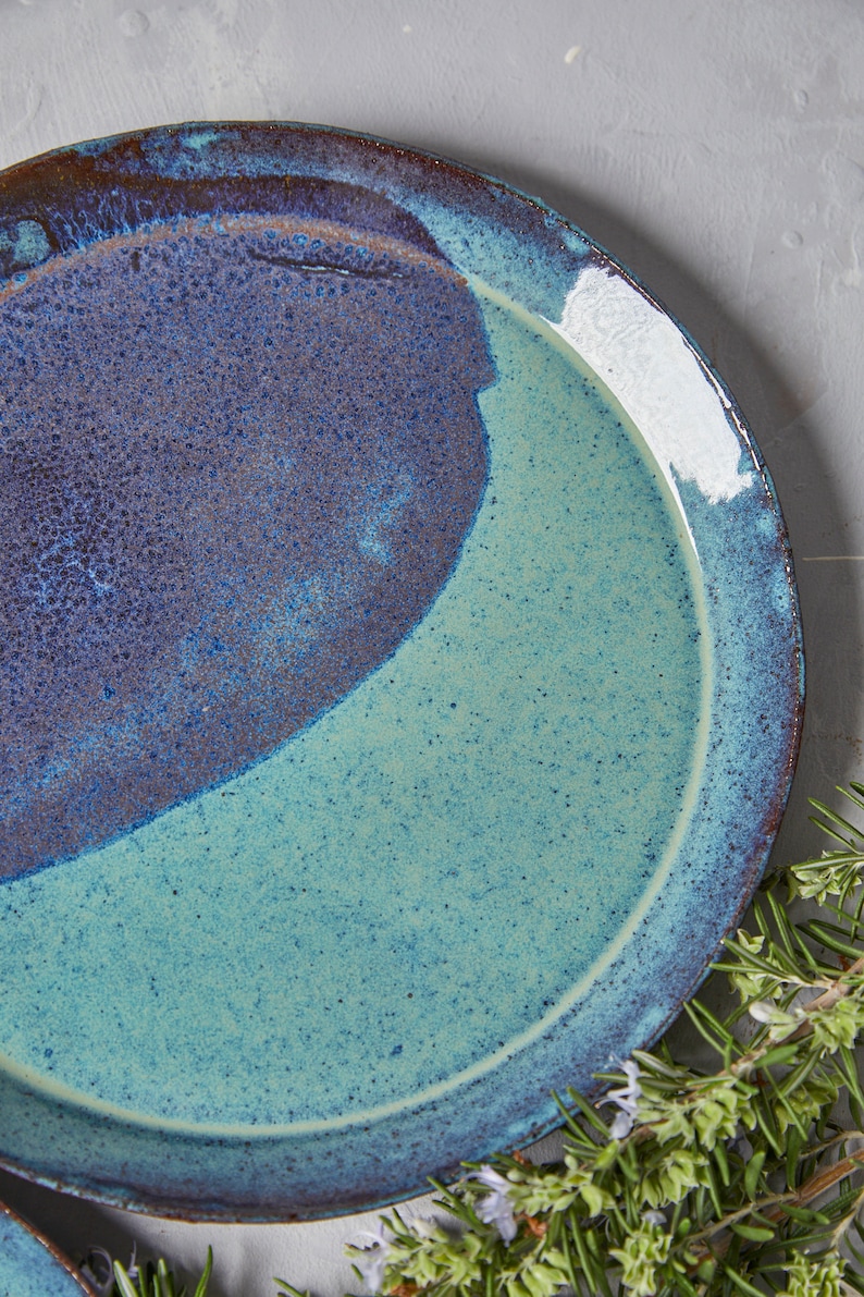 May include: A ceramic plate with a blue and green glaze. The plate has a speckled finish and a rounded rim.