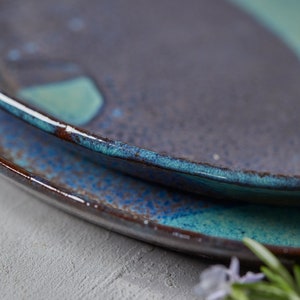 May include: Two ceramic plates with a blue and brown glaze. The plates are stacked on top of each other. The top plate has a light blue glaze with a darker blue rim. The bottom plate has a darker blue glaze with a brown rim.