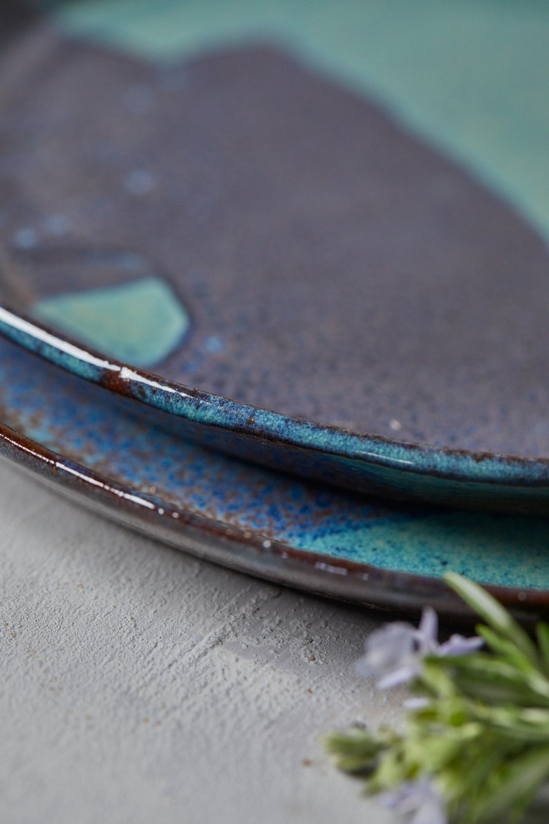 May include: Two ceramic plates with a blue and brown glaze. The plates are stacked on top of each other. The top plate has a light blue glaze with a darker blue rim. The bottom plate has a darker blue glaze with a brown rim.