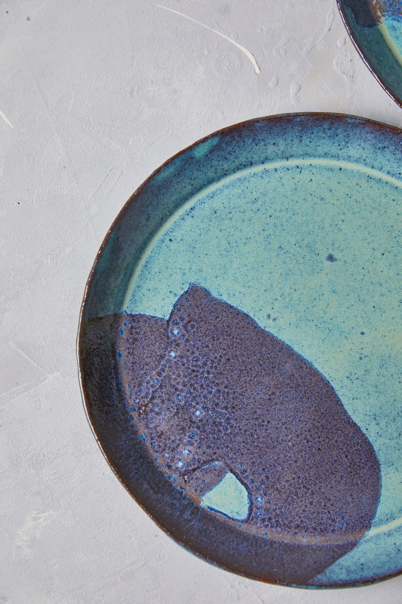 May include: A round ceramic plate with a blue and brown glaze. The plate has a unique design with a dark brown section on one side and a light blue section on the other side.
