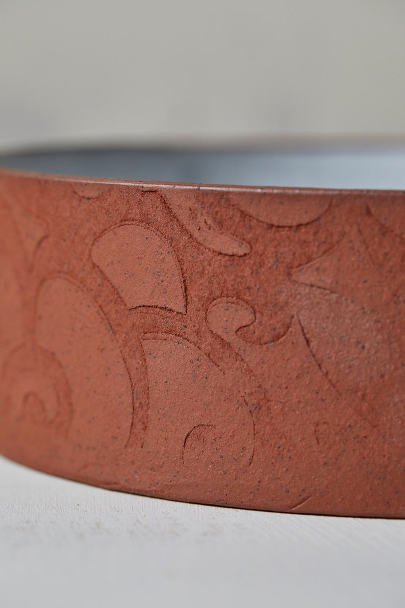 May include: Close-up of the rim of a terracotta-colored ceramic bowl with a decorative pattern of swirls and dots.