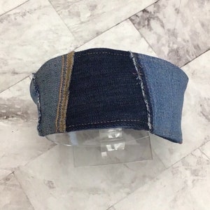 May include: A denim headband made from different shades of blue denim fabric. The headband is sewn together with a contrasting brown thread.