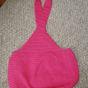 May include: A handmade, bright pink crochet tote bag with a unique teardrop shape. The bag features a long, looped handle and a textured stitch pattern. This stylish bag is perfect for carrying essentials.