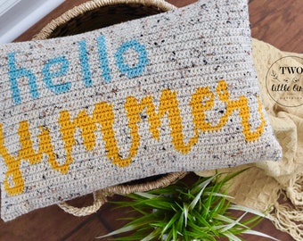 May include: A crocheted pillow with the words "hello summer" in blue and yellow lettering on a white background with speckles of color.