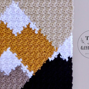 May include: A close-up of a crocheted blanket with a geometric pattern in shades of beige, white, mustard yellow, and black. The blanket is made with a textured stitch and has a modern, minimalist design.